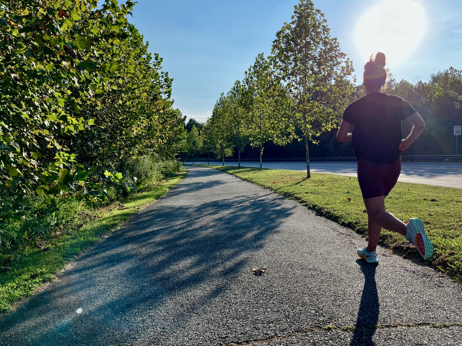 person in right of frame runs down paved pedestrian path with green trees on either side