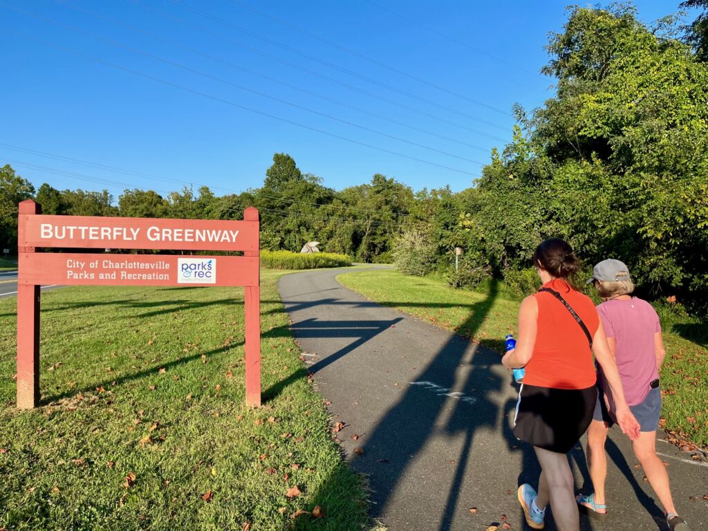 two women in pink shirts walk on path next to sign that says Butterfly Greenway