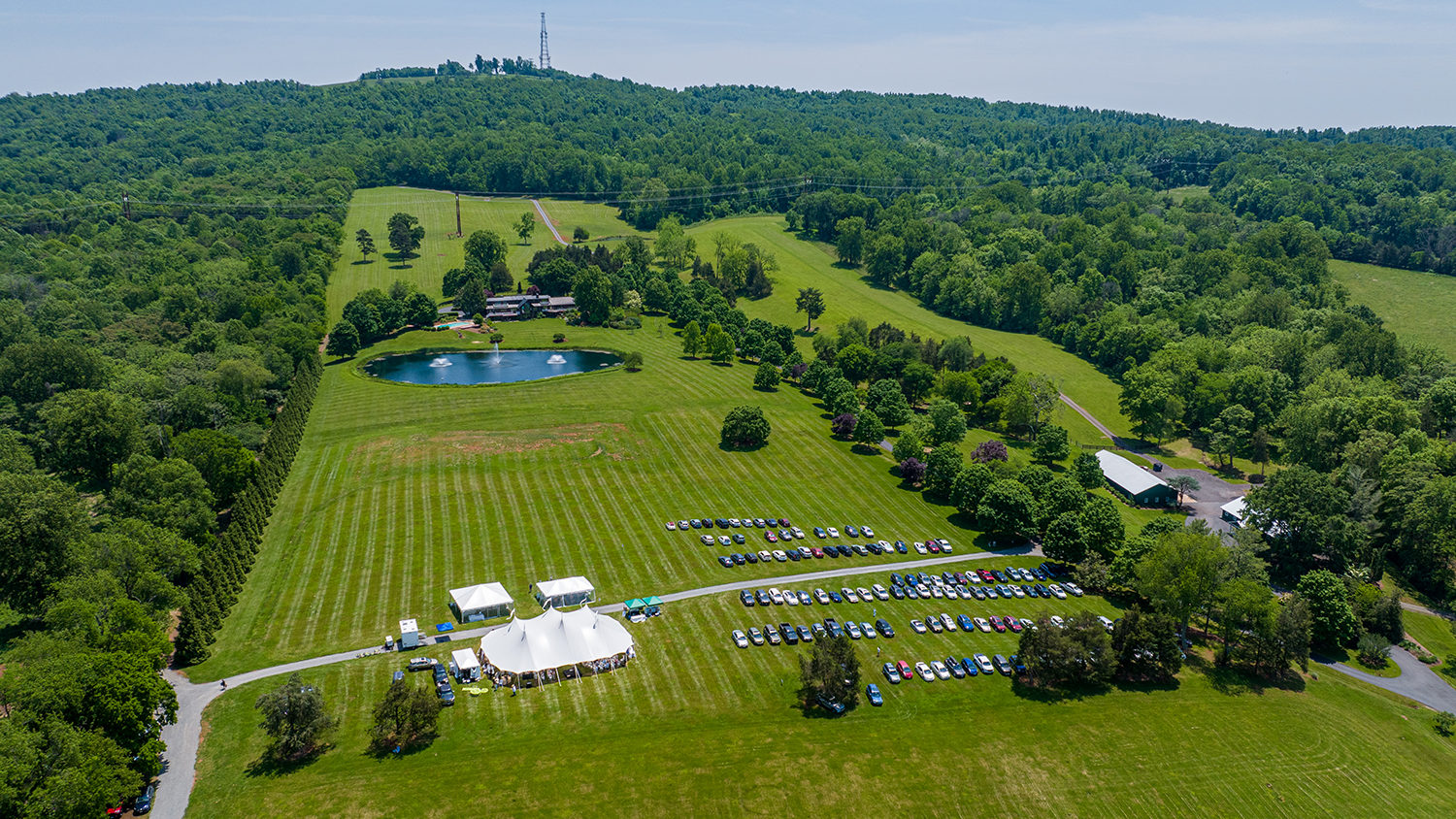 aerial image of a large lawn at the top of a mountain, with an event tent and parked cars