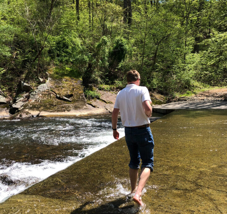 man in white shirt and blue jeans walks through flowing stream