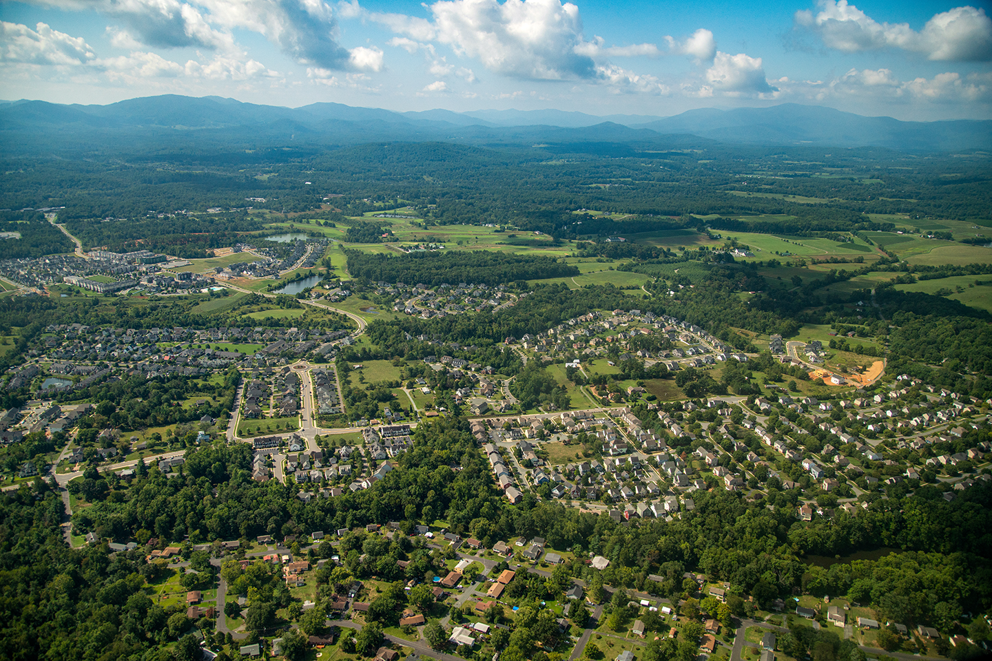 aerial image of suburban neighborhoods surrounded by green forest canopy, blue mountains and cloudy skies